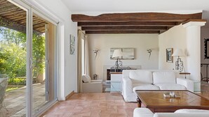 Amplia sala de estar con chimenea, muebles blancos y vistas a un patio exterior por una puerta de cristal.