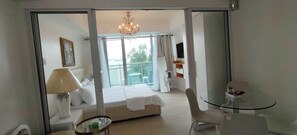 A hotel room with a bed, a glass table, a chair, a lamp, a TV, and a balcony with a view. - Azure Urban Resort - Serene 1-BR condo good for 4 PAX (Para)
