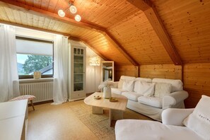 Une pièce chaleureuse avec un plafond en bois, des meubles blancs et une grande fenêtre agrémentée de rideaux.