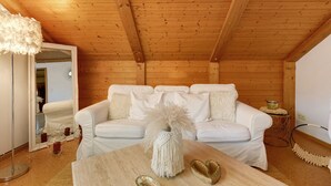 Een witte bank met een decoratieve witte vaas, een houten plafond en een spiegel aan de linkerkant.