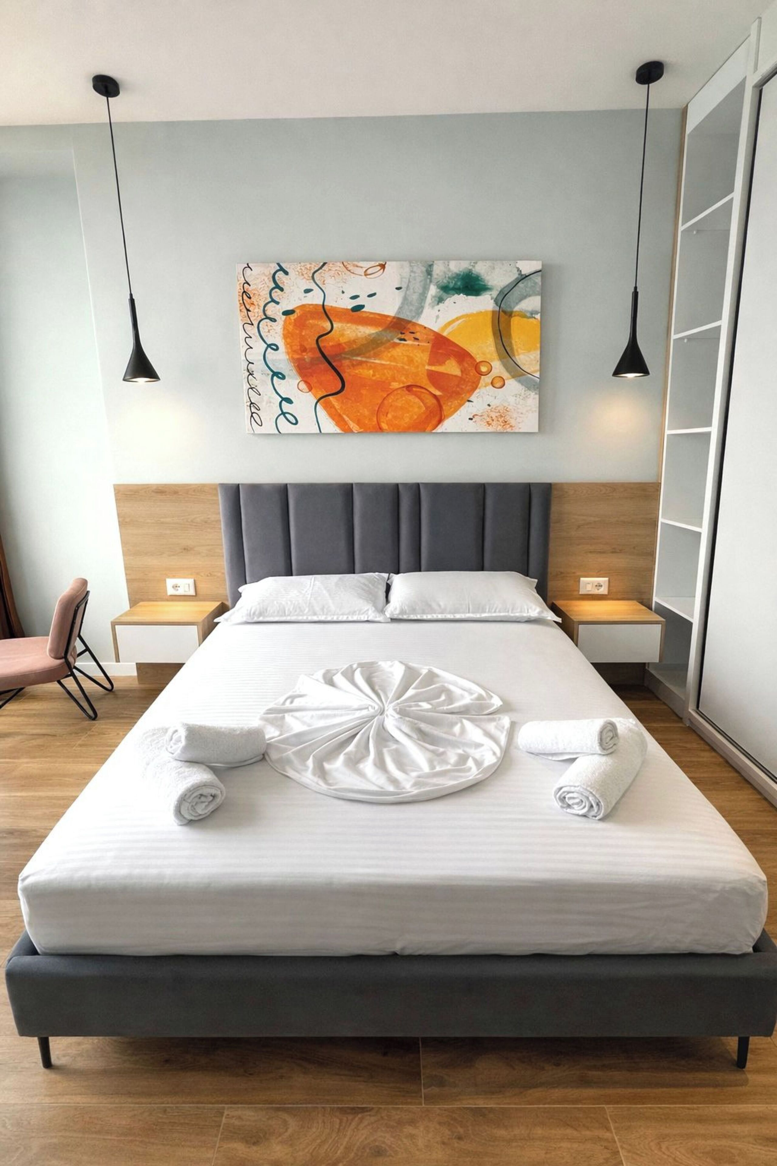 A modern hotel room with a large bed, two bedside tables, a chair, and a wall-mounted artwork.