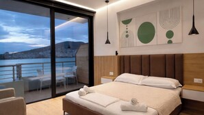 Ein modernes Schlafzimmer mit einem großen Bett, einem Balkon mit Blick auf das Wasser und abstrakter Wandkunst.
