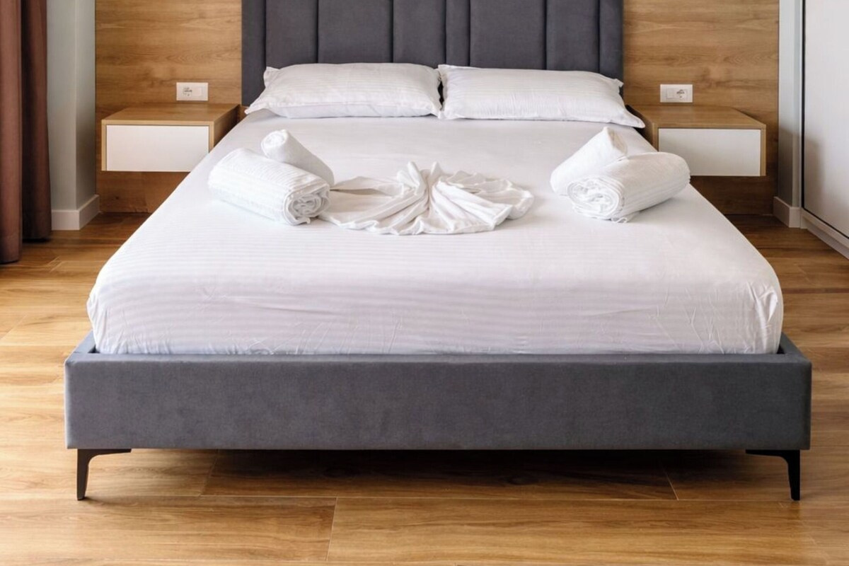 A modern hotel room with a large bed, wooden headboard, and two bedside tables.
