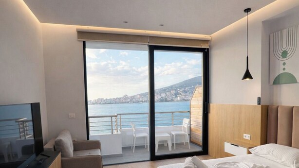 Ein modernes Schlafzimmer mit einem großen Bett, einem Fernseher, einer Couch und einem Balkon mit Meerblick.