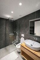 Un baño moderno con ducha de vidrio, inodoro blanco y tocador de madera con lavamanos grande.
