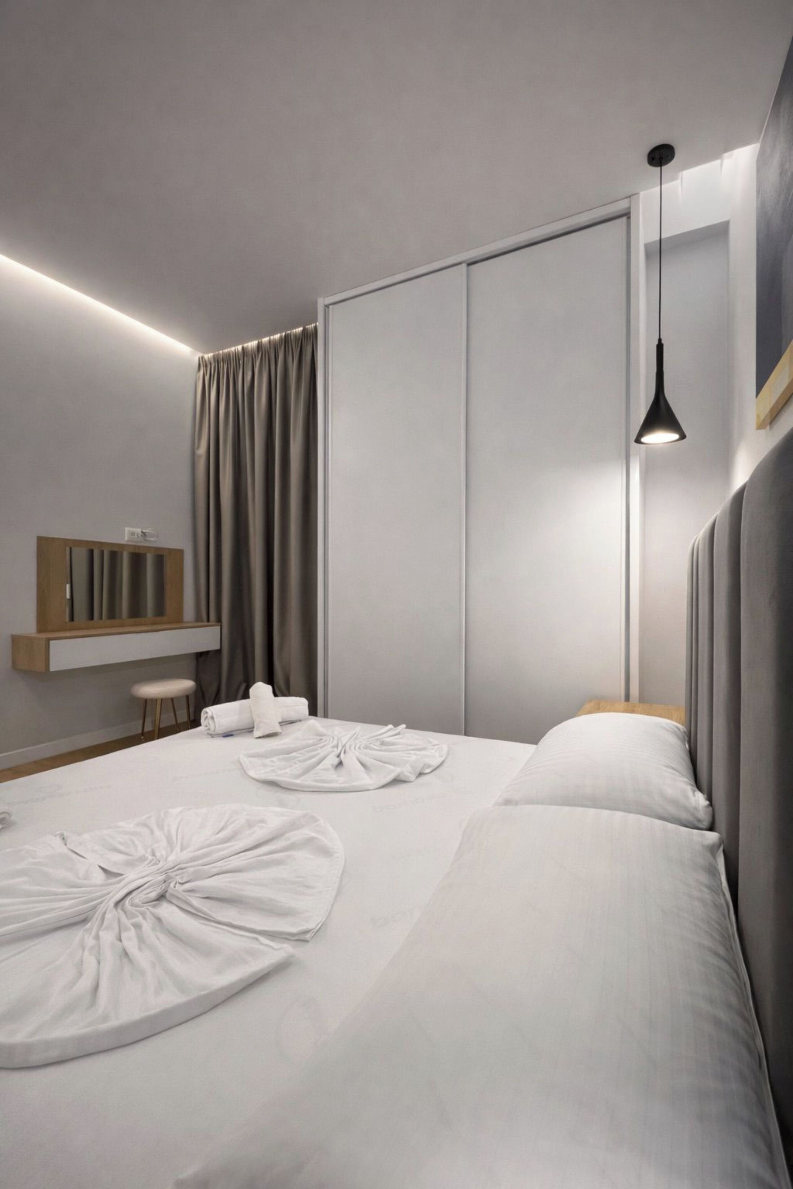 A modern hotel room with a large bed, a bedside table, a mirror, and a hanging light fixture.