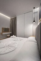 Una habitación de hotel moderna con una cama grande, una mesita de noche, un espejo y una lámpara colgante.