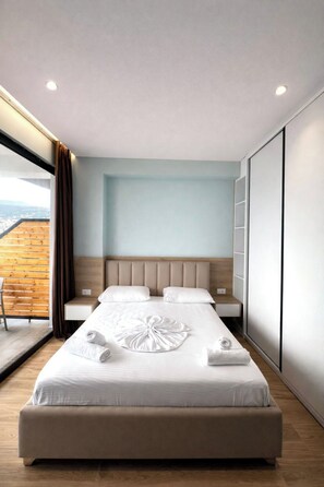 A modern hotel room with a large bed, a wooden ceiling, and a view of the city. - Hotel Tramonto (Sarande)
