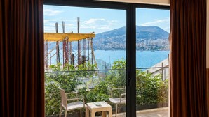 Ein Zimmer mit einer großen Schiebeglasdoor, die auf einen Außenbalkon mit Blick auf eine Stadt und ein Gewässer führt.