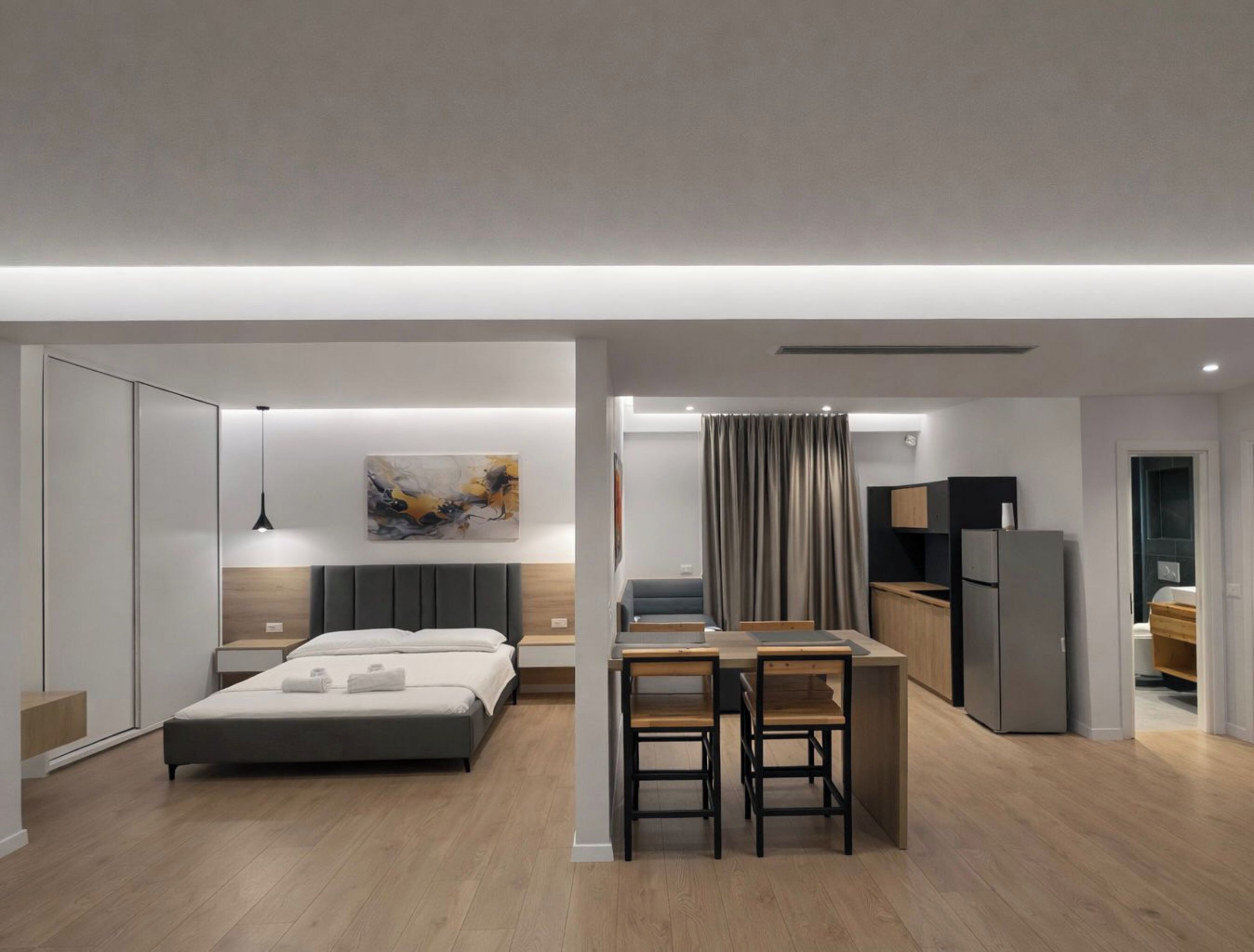 Een moderne, compacte hotelkamer met een bed, nachtkastjes, een bureau met stoelen, een kitchenette en een badkamer.