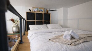 Un dormitorio con una cama, una mesita de noche de madera, una estantería con fotos y una planta pequeña.