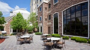 An outdoor patio with brick flooring, outdoor seating, and a large window on the building. - 2 Spacious Suites Near Mall of America & MSP Airport with Breakfast Included (Bloomington)