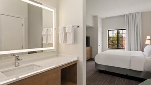 A modern hotel room with a large mirror, a wooden vanity, a bed, and a window with curtains. - 2 Spacious Suites Near Mall of America & MSP Airport with Breakfast Included (Bloomington)