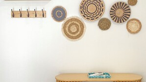 A room with a wooden table, a woven basket, and a wall-mounted shelf with decorative items.