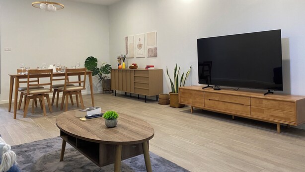 A modern living room with a dining area, a flat-screen TV, wooden furniture, and a ceiling fan.