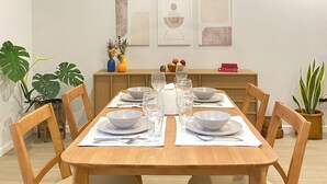 A dining area with a wooden table set for four, surrounded by chairs. There are three wall-mounted artworks above the table.