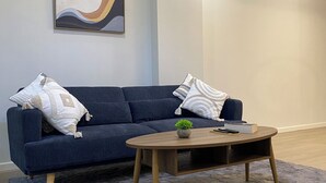 A modern living room with a dark blue sofa, a round wooden coffee table, and a grey shaggy rug.