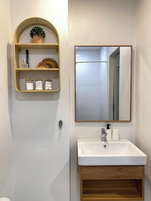 Une salle de bain avec un lavabo blanc, un meuble-lavabo en bois, un miroir et une étagère contenant des articles de toilette.