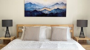 A hotel room with a large bed, two bedside tables with lamps, and a painting of mountains on the wall.
