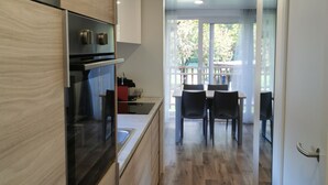 Een moderne keuken met houten kastjes, een inbouwoven en een eethoek met een tafel en stoelen.