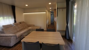 Een moderne woonkamer met een hoekbank, een houten eettafel en een keuken op de achtergrond.