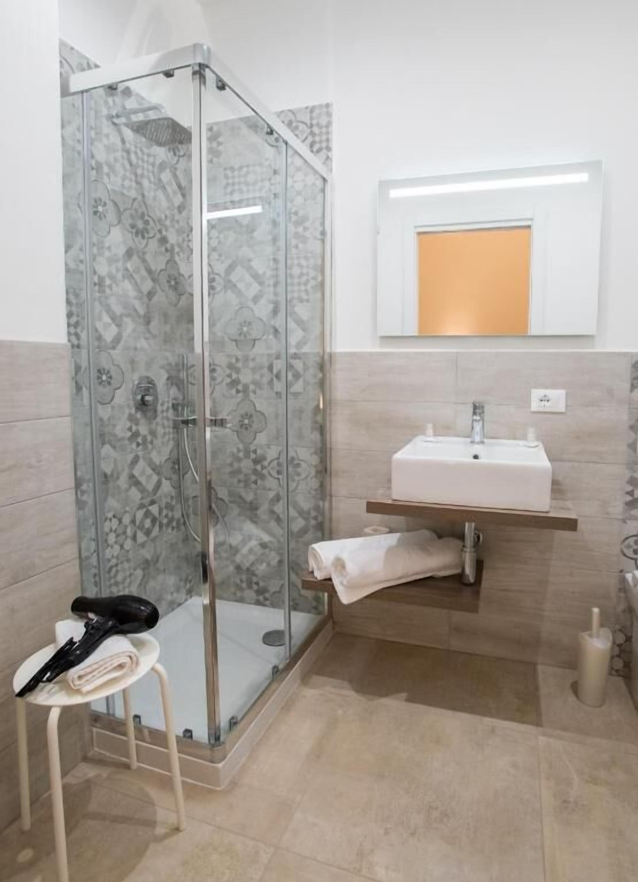 A modern bathroom with a glass shower enclosure, a white sink, and a towel rack.
