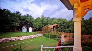 A covered outdoor area with a view of a grassy yard, a small pond, and a red-roofed building.