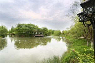 A calm river with a wooden dock, lush greenery, and a traditional-style lamp post.