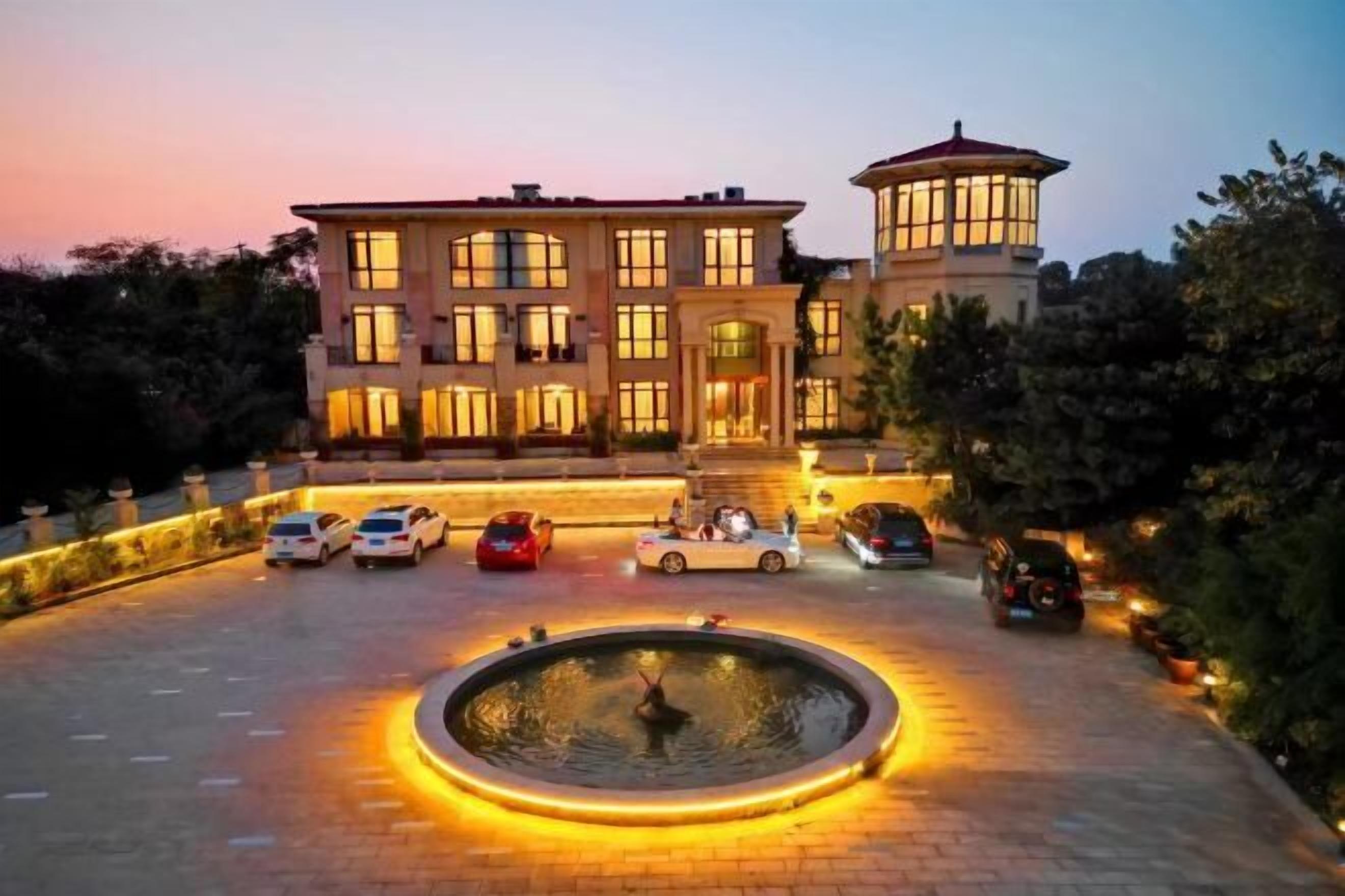 A large, multi-story building with a circular fountain in the center, surrounded by parked cars.
