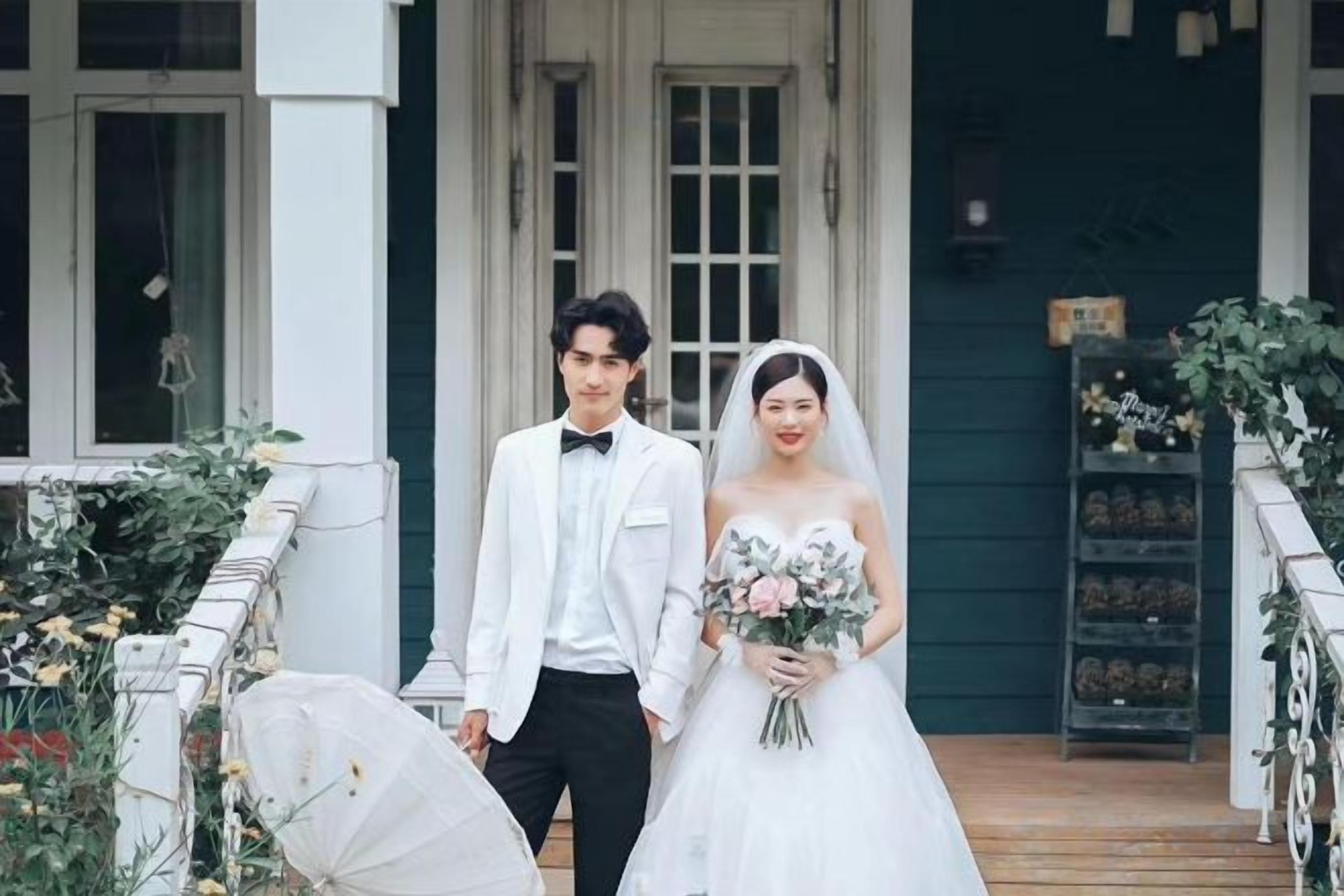 A couple in wedding attire standing in front of a building with a porch.