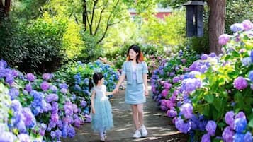 A pathway surrounded by vibrant flowers, a person and a child walking, and a lamp post in the background.
