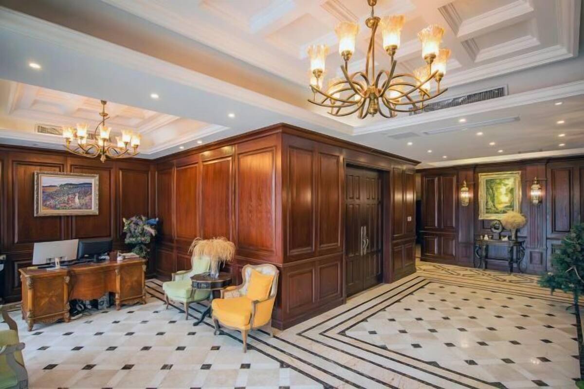 A spacious lobby with a checkered floor, wooden paneling, a reception desk, and a large chandelier.