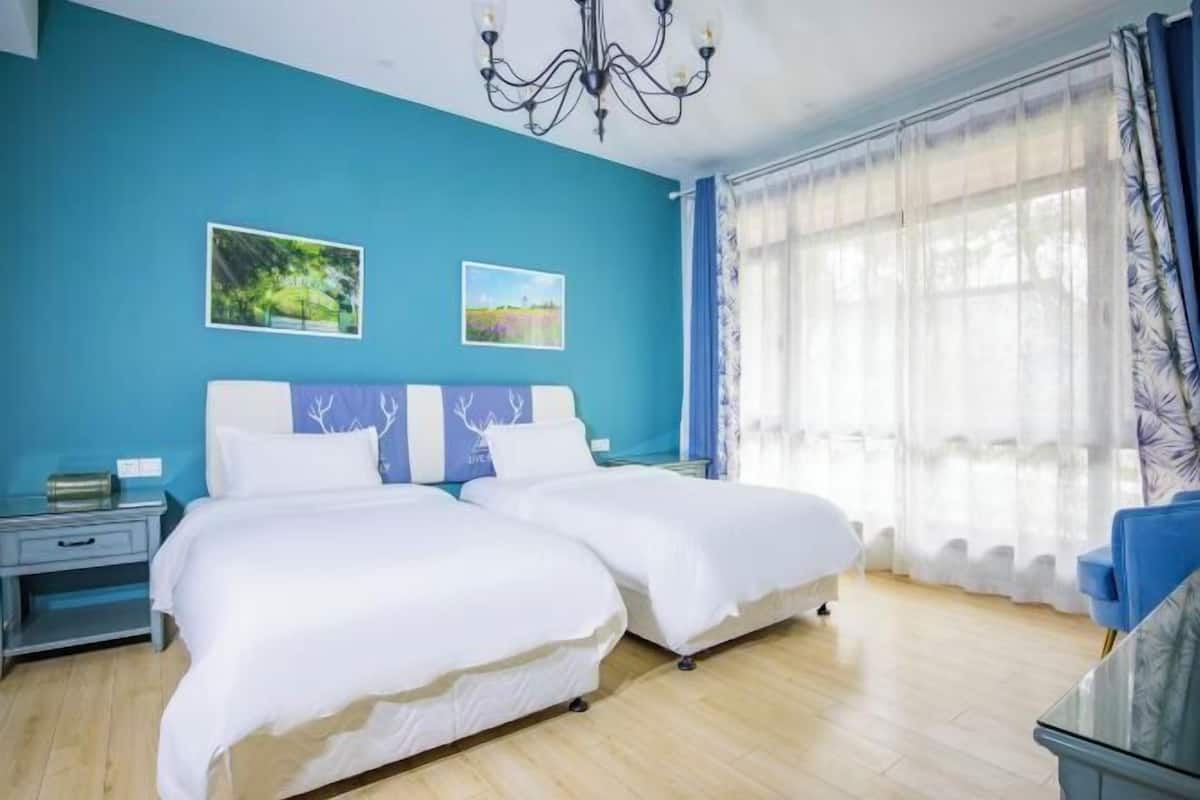 A room with two beds, a chandelier, a nightstand, and a window with curtains.