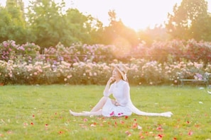 A person sitting on grass in a garden with flowers and trees in the background.
