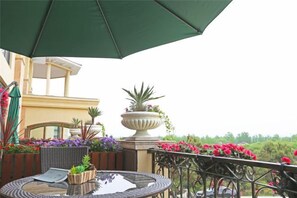 Eine Terrassengruppe im Freien mit rundem Tisch, Stühlen, einem grünen Sonnenschirm und Kübelpflanzen.