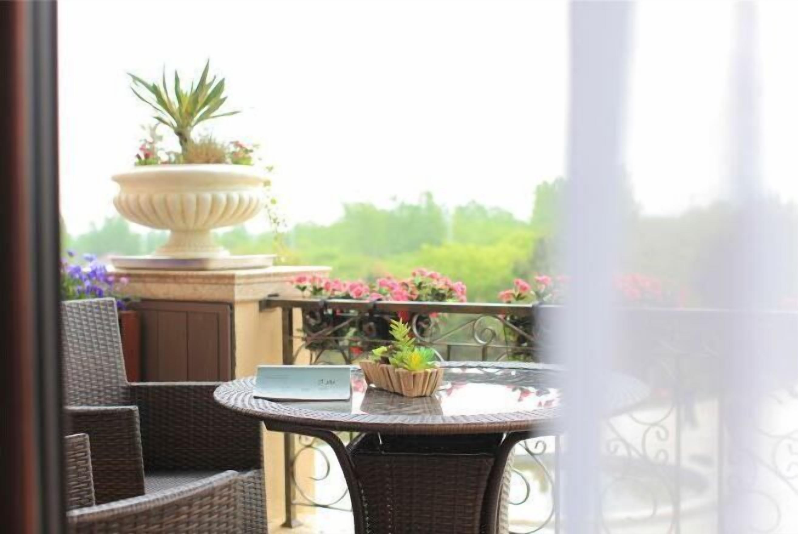 A balcony with wicker furniture, a round table, and a decorative urn with plants.