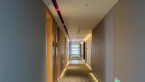 A long, narrow hotel corridor with carpeted floors, wooden walls, and a ceiling with recessed lighting.