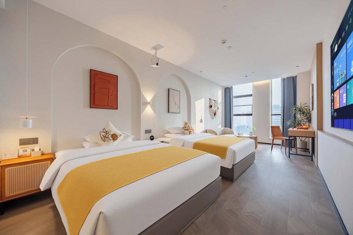 A hotel room with two beds, a desk, and a TV.