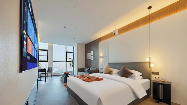 A modern hotel room with a large bed, a desk, and a view of the city.