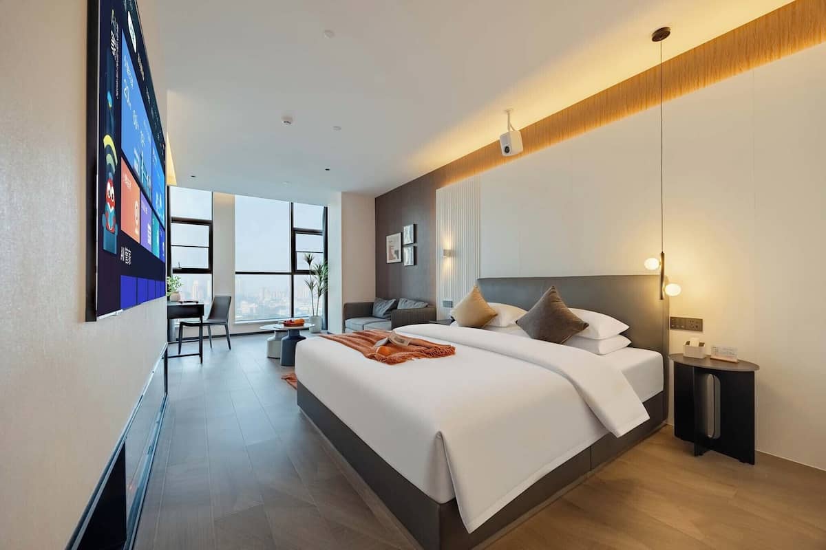A modern hotel room with a large bed, a desk, and a view of the city.