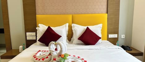 A hotel room with a bed, two pillows, a red blanket, and two towels shaped like swans with flowers.