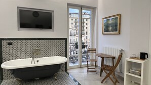 Une salle de bain avec une baignoire sur pieds, un téléviseur fixé au mur, une chaise, une petite table et un radiateur.