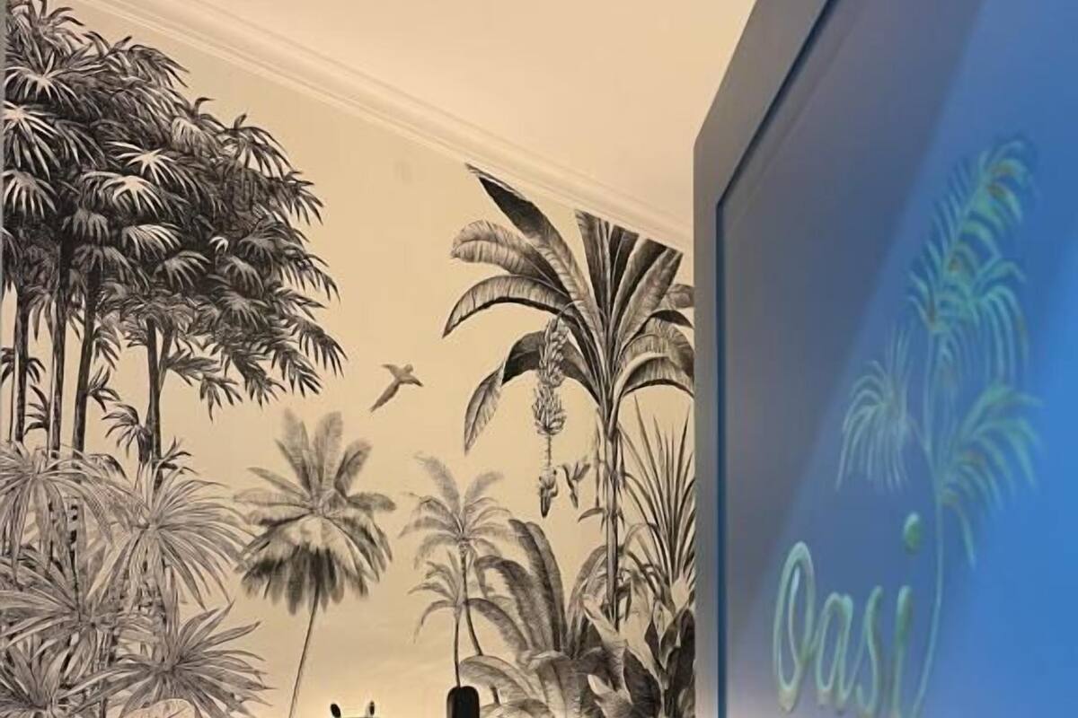 Un dormitorio con cama, almohadas, mesita de noche y un mural de plantas tropicales.