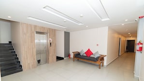 A modern lobby with a staircase, a sofa with cushions, a fire extinguisher, and a door with an elevator. - The Royal Samrat Residency (karnataka)