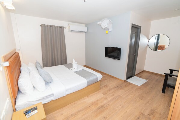 Habitación de hotel con cama, televisión, aire acondicionado, espejo y suelo de madera.