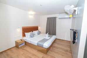 Habitación de hotel ordenada con una cama de madera, una mesita de noche, aire acondicionado de pared y ventilador de techo.