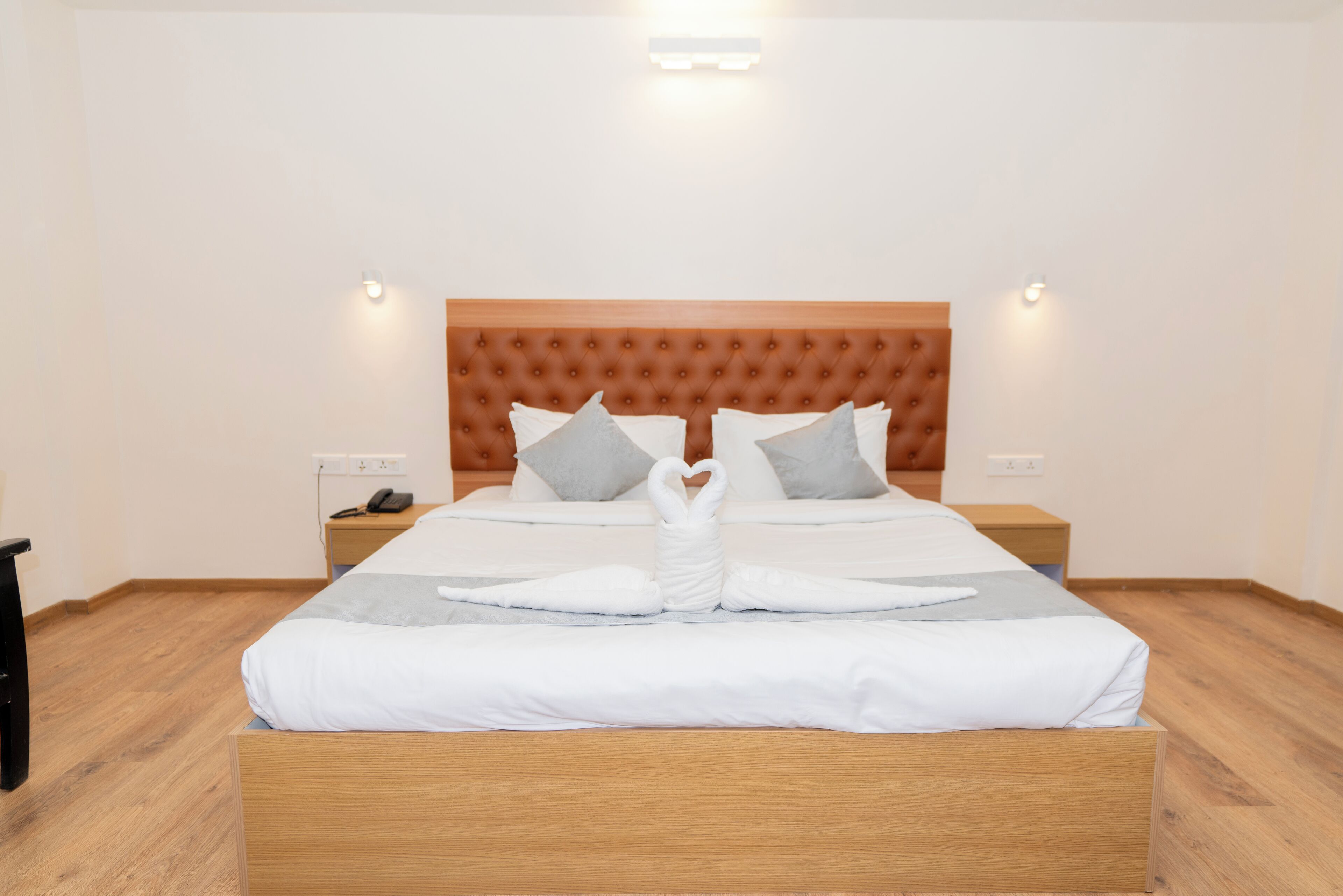 A neatly made bed with a wooden headboard, white bedding, and two pillows. There are bedside tables with lamps and a phone on one side.
