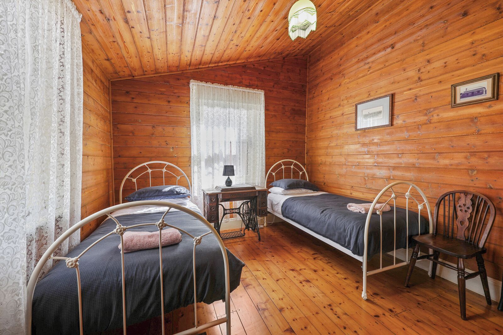 Une pièce de cabane en bois comprenant deux lits en métal, une petite table et une chaise.