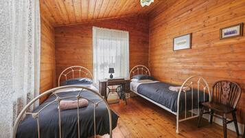 Une pièce de cabane en bois comprenant deux lits en métal, une petite table et une chaise.