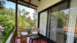 Un balcón con dos sillas de mimbre y una mesita, con vistas a un jardín exuberante con palmeras.